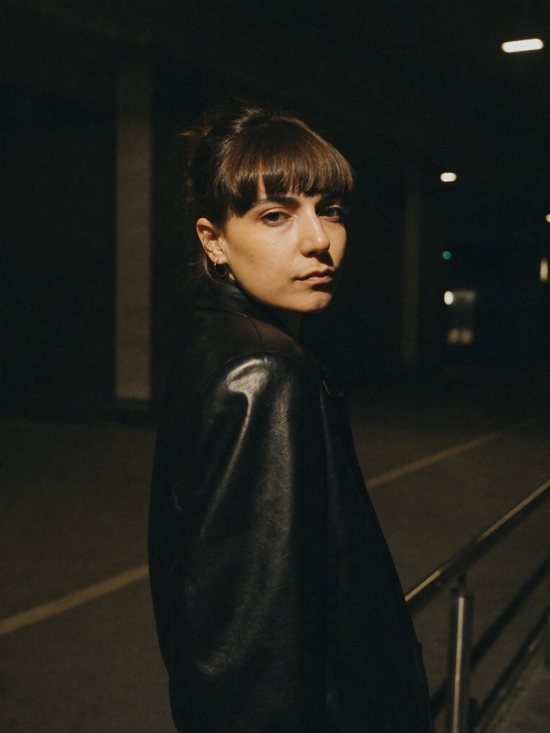Elene looking toward the camera at night in a black leather jacket