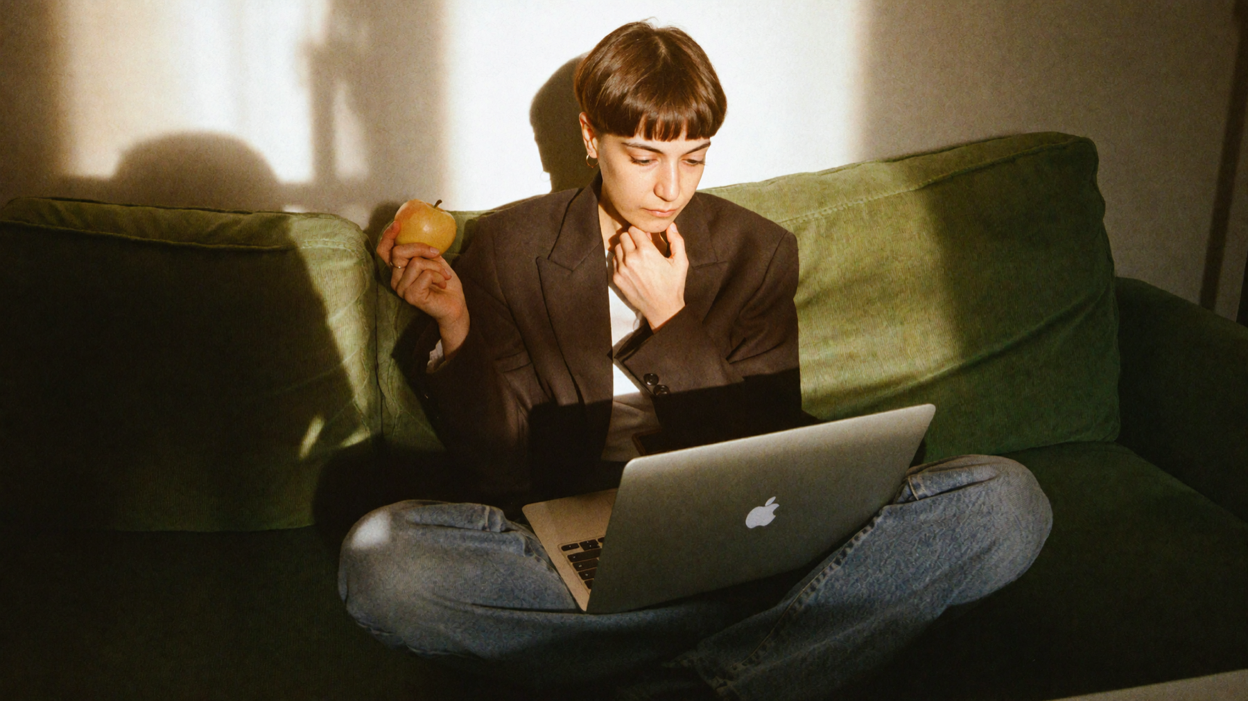 Elene sitting on a green sofa with a laptop in warm sunlight